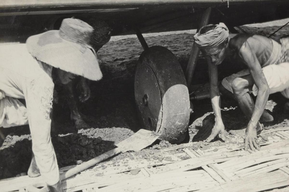 Local villagers lay panels from their bamboo huts underneath the bogged wheels of the Vickers Vimy aircraft in Surabaya, Indonesia, 1919