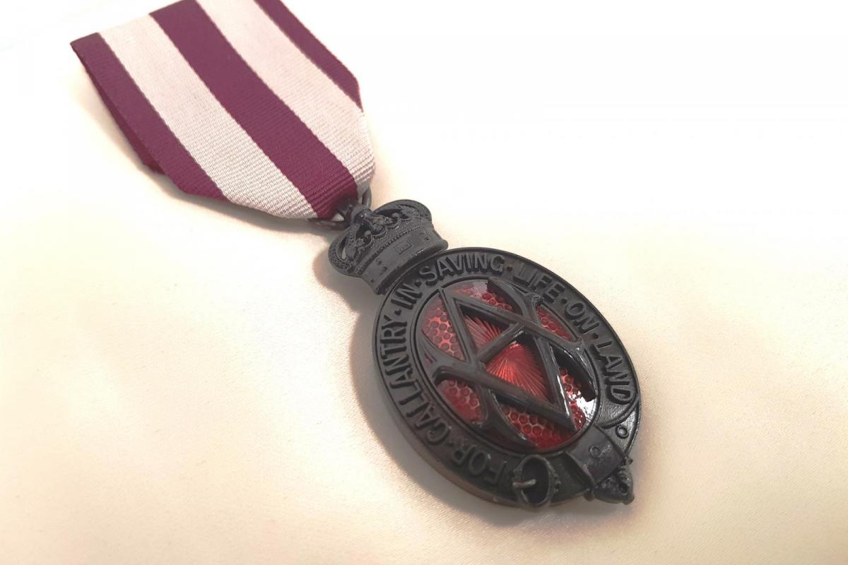 Albert medal. Ribbon is striped maroon and white. Medal is made of bronze with red embelishments