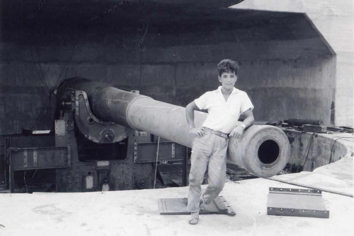 A young member of the Fujita Salvage Company leans against a 9.2-inch counter-bombardment gun at East Point.