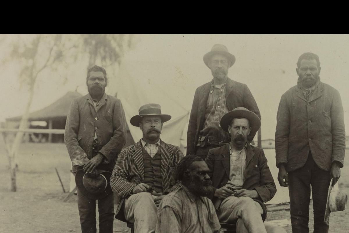 Depicts three Aboriginal men and three non-Aboriginal men posing for the camera in front of their camp.