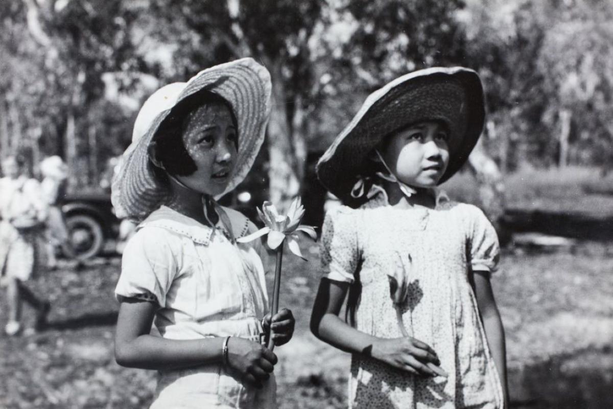 Black and white photo. Two girls wearing sunhats and holding water lilies 