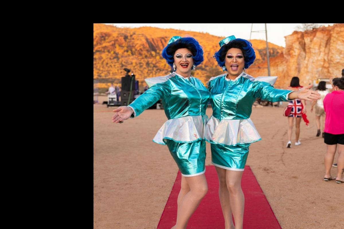 Two well-dressed and welcoming “hostesses” in short satin skirts on the red carpet in front of a windmill and desert range.