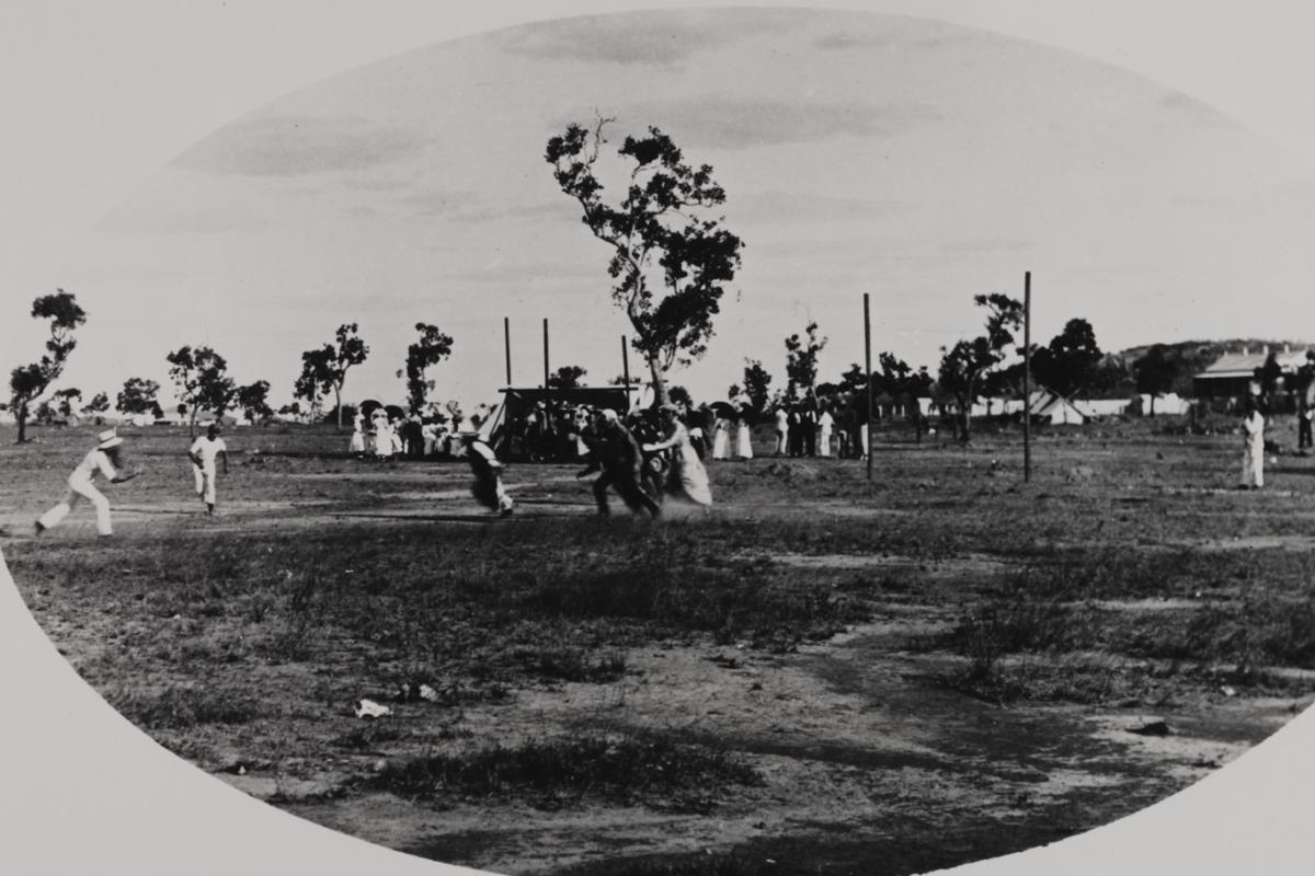 Blurred image of half a dozen distant figures in various costumes on a sporting field with small crowd in background.