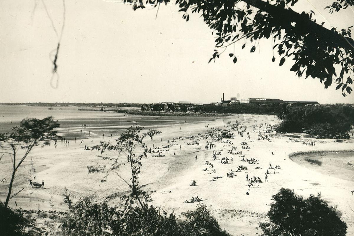 Photograph from afar of people on the sandy beach by the water.