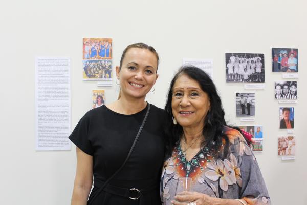Two women standing in front of exhibition smiling at the camera