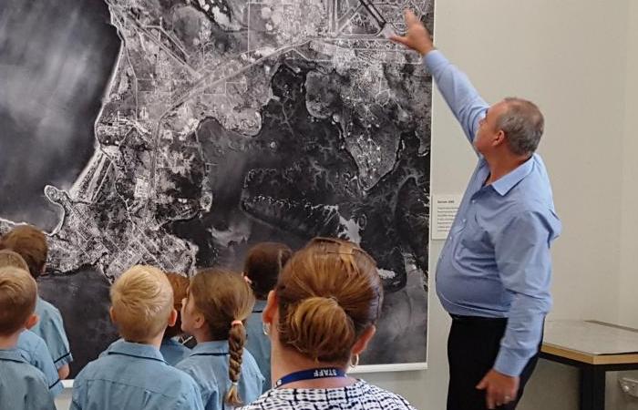 Group of students facing a man who is pointing to a large aerial photo 