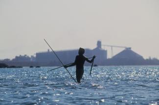 Man fishing in waters in front of processing plant.