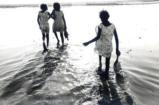 Black and white photograph of three people wading through water, carrying turtles.