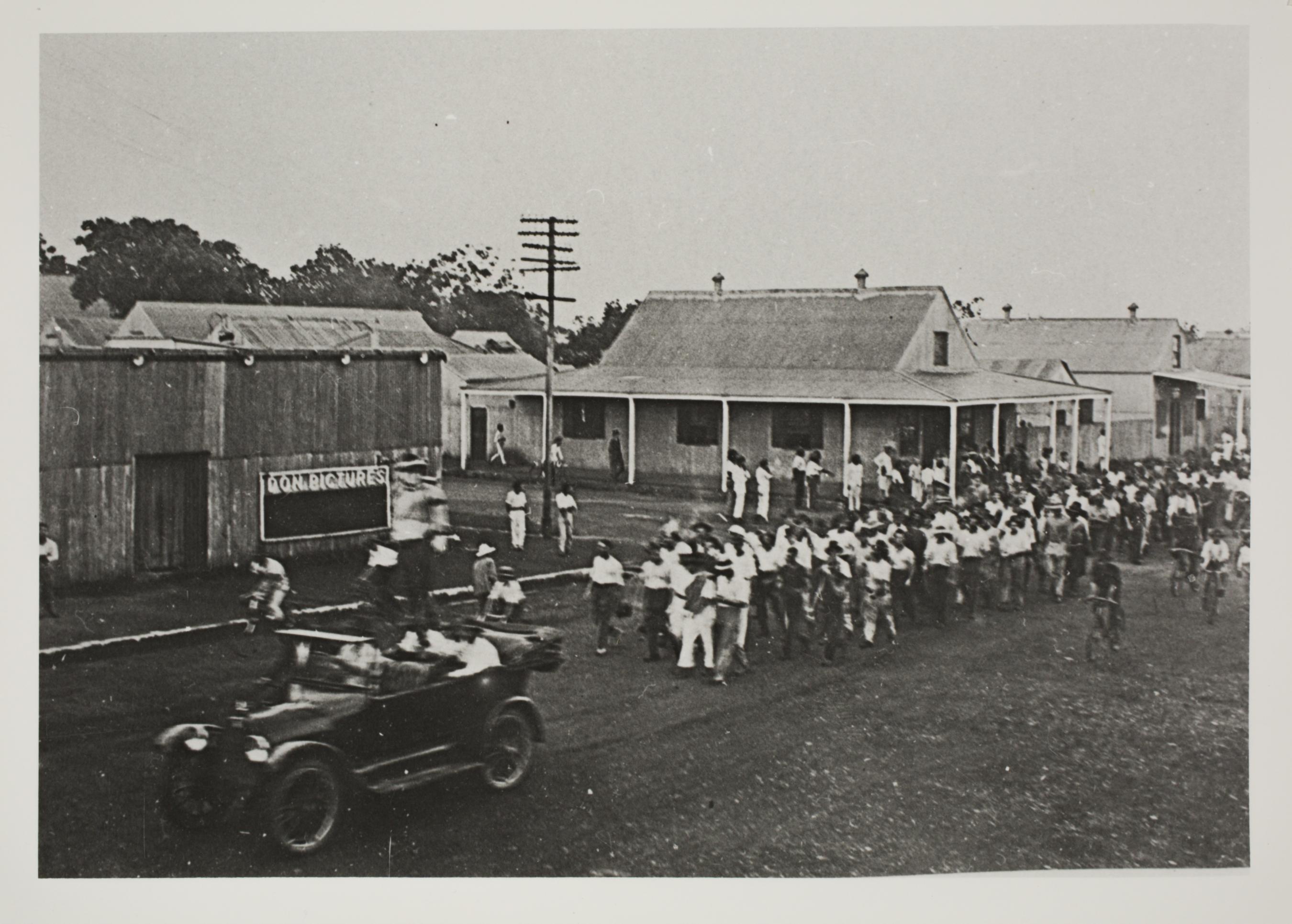 Black and white photo of a protest led by a motor vehicle and followed by a group of people in 1918