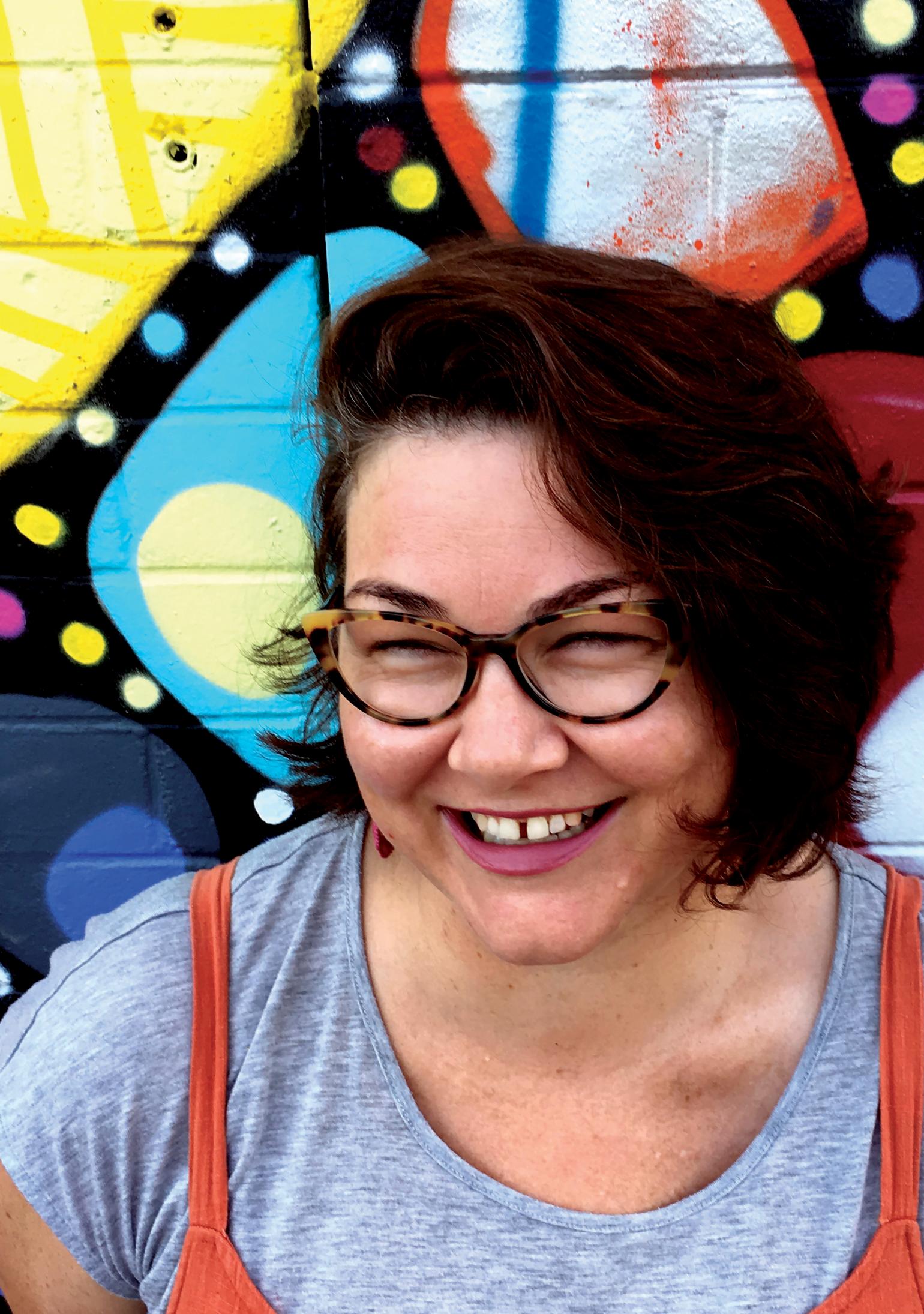 Woman laughing, standing in front of graffiti wall