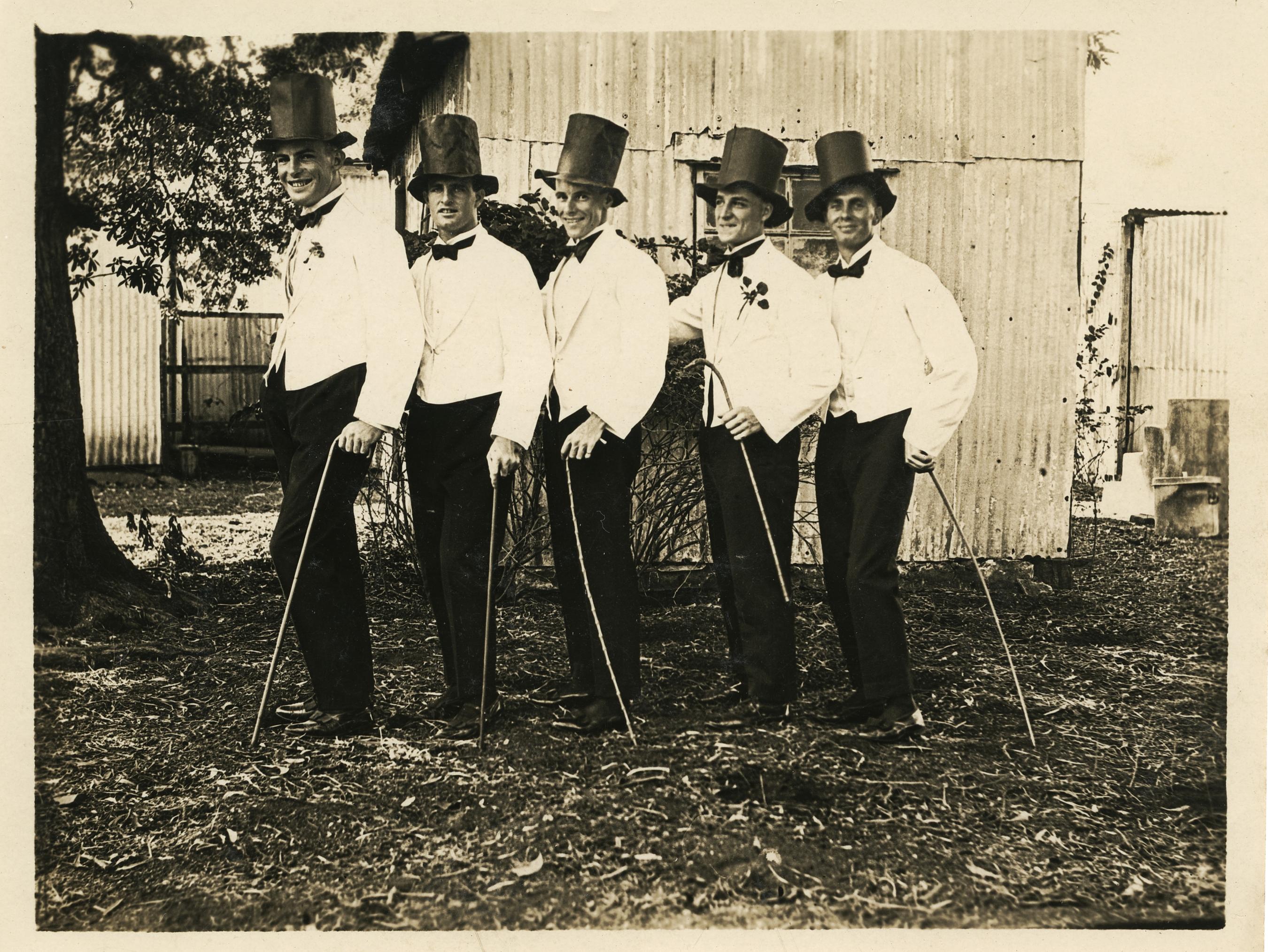 black and white photo of five men in top hats, suits and canes in a row