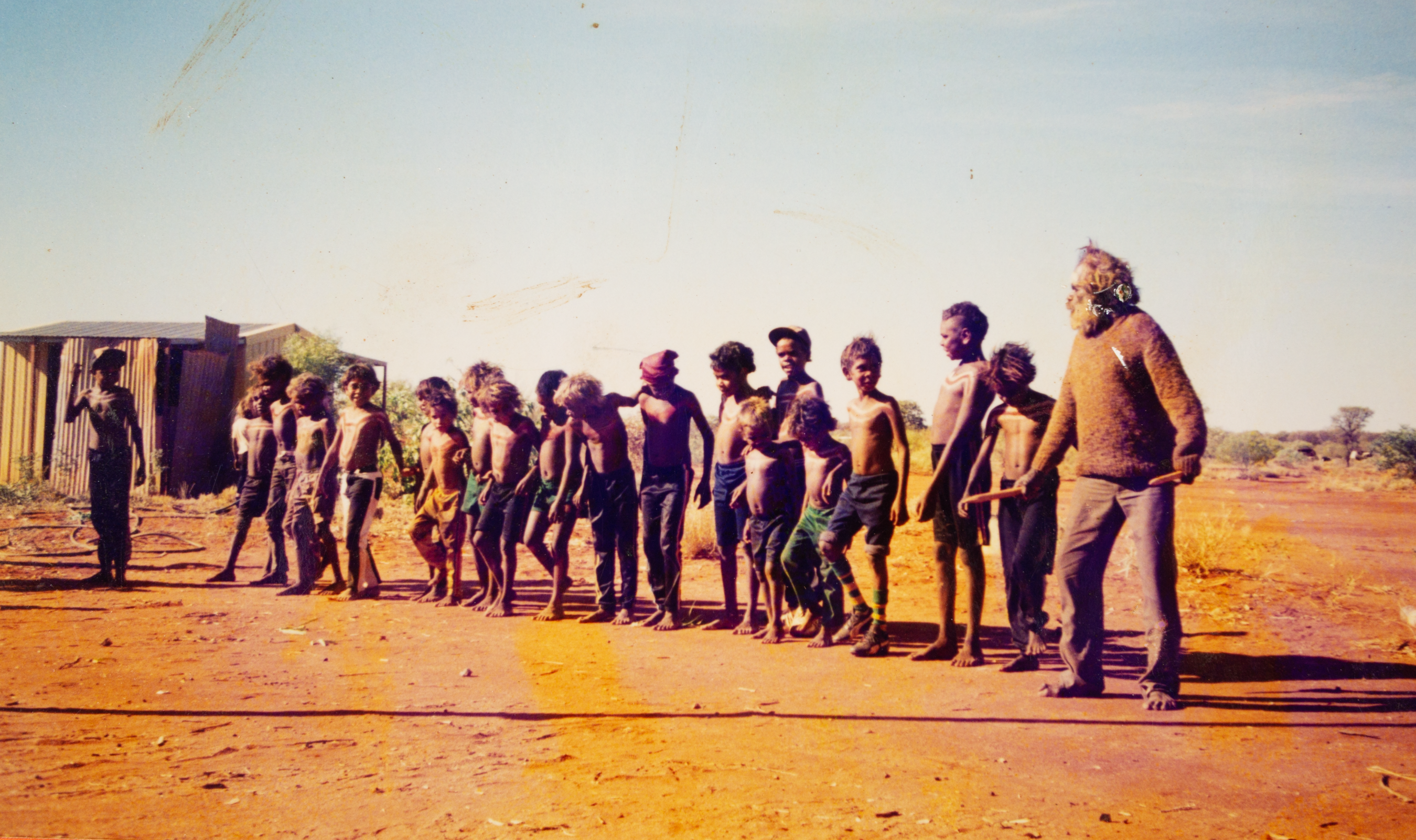 Photograph of boys and men standing together against a backdrop of blue sky and red earth