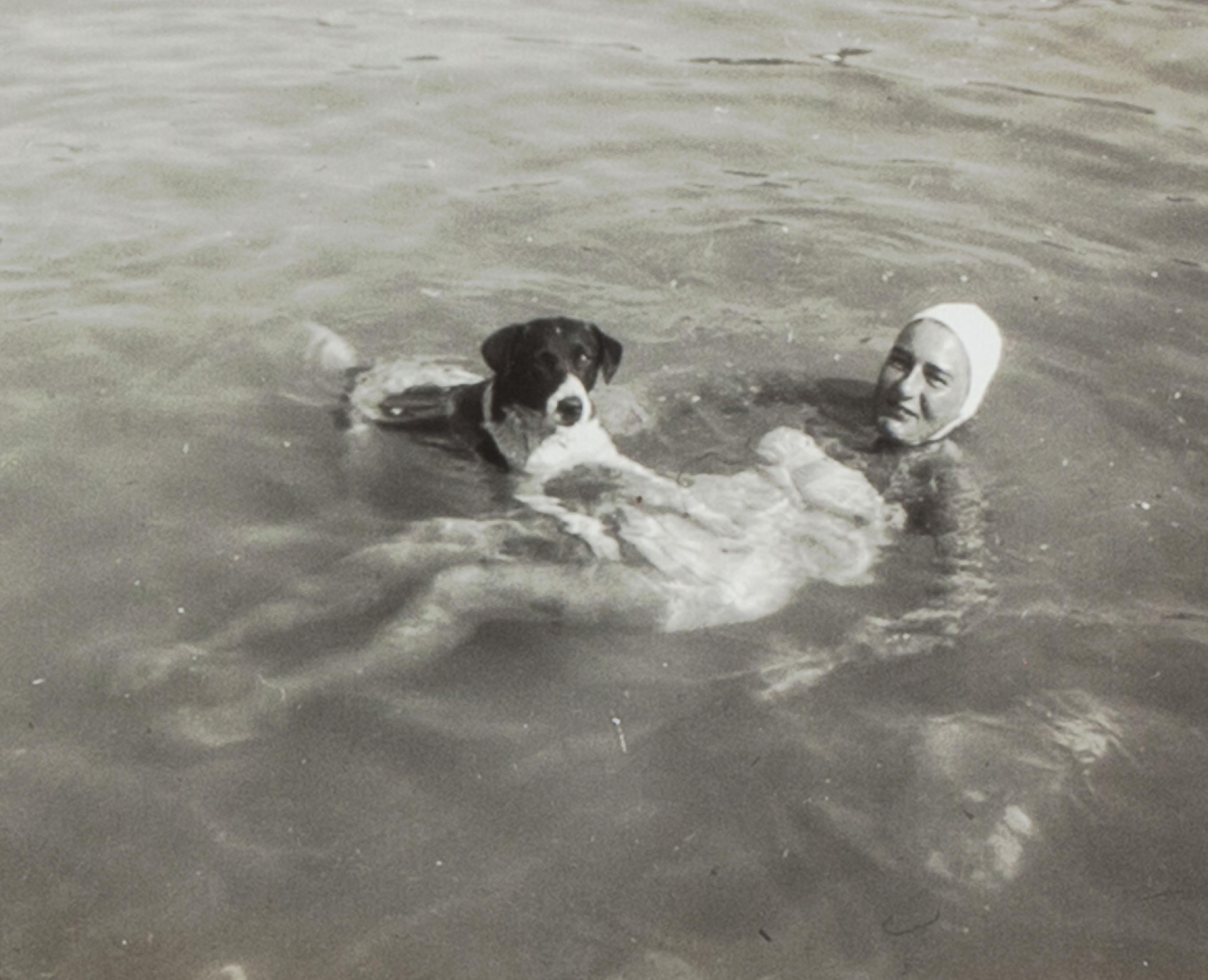Black and white photograph of woman and dog swimming.