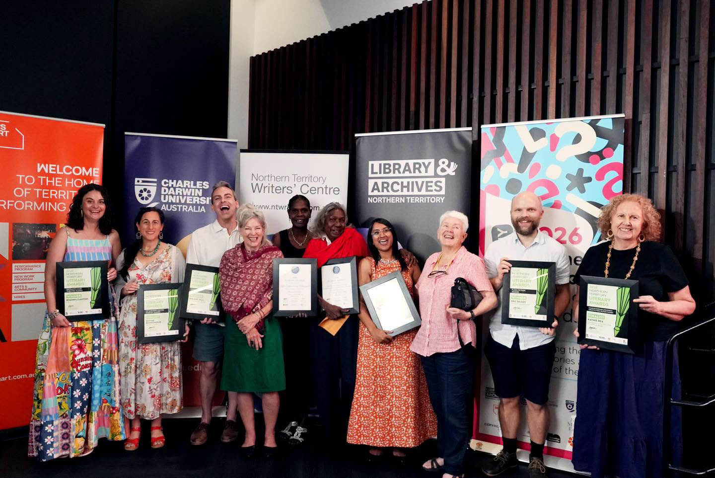 Photograph of 10 finalists holding certificates in frames standing in front of banners.