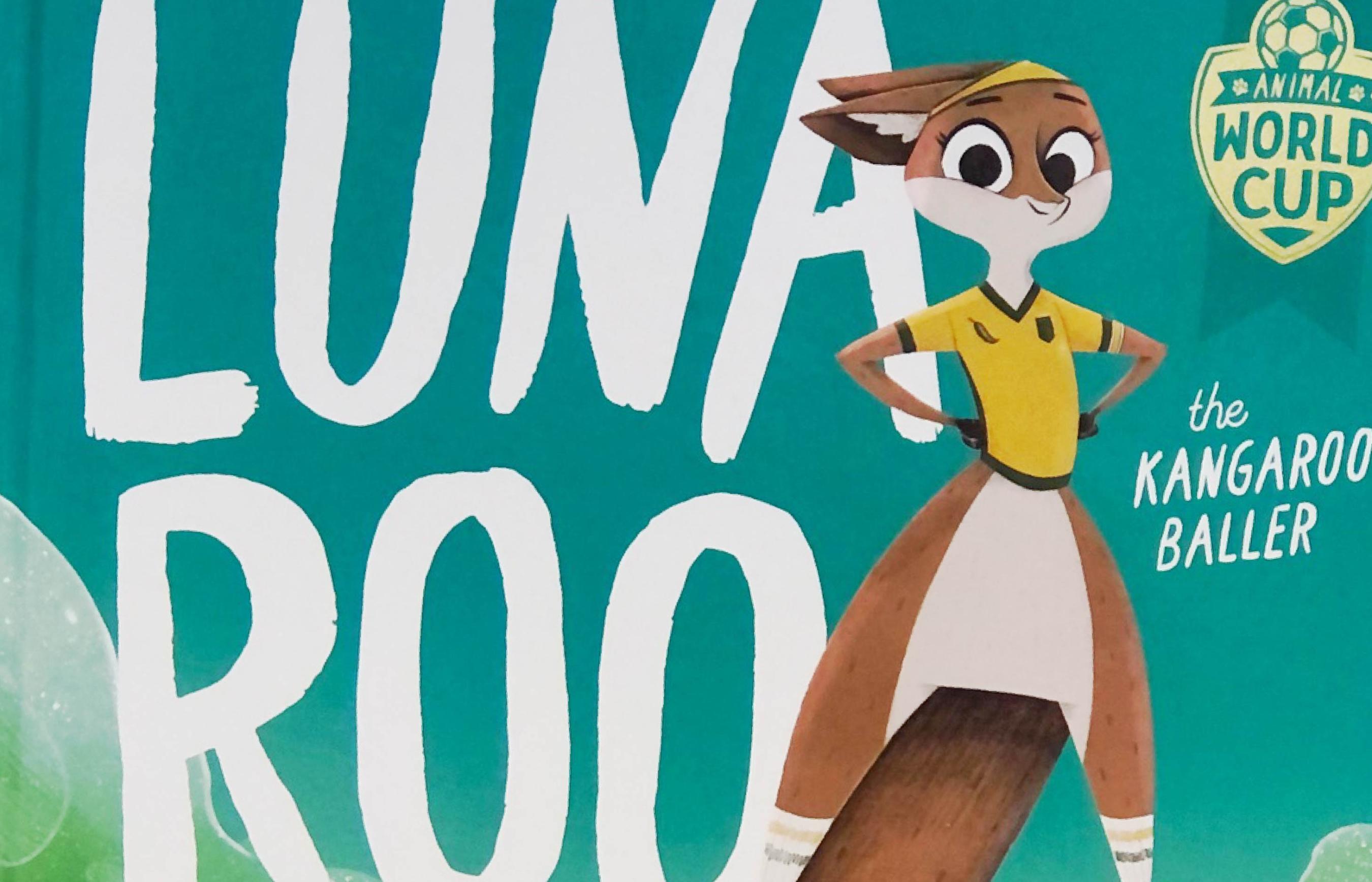 Photo of section of 'Luna Roo' book cover, teal-green background and white text, featuring illustrating of kangaroo in a yellow shirt