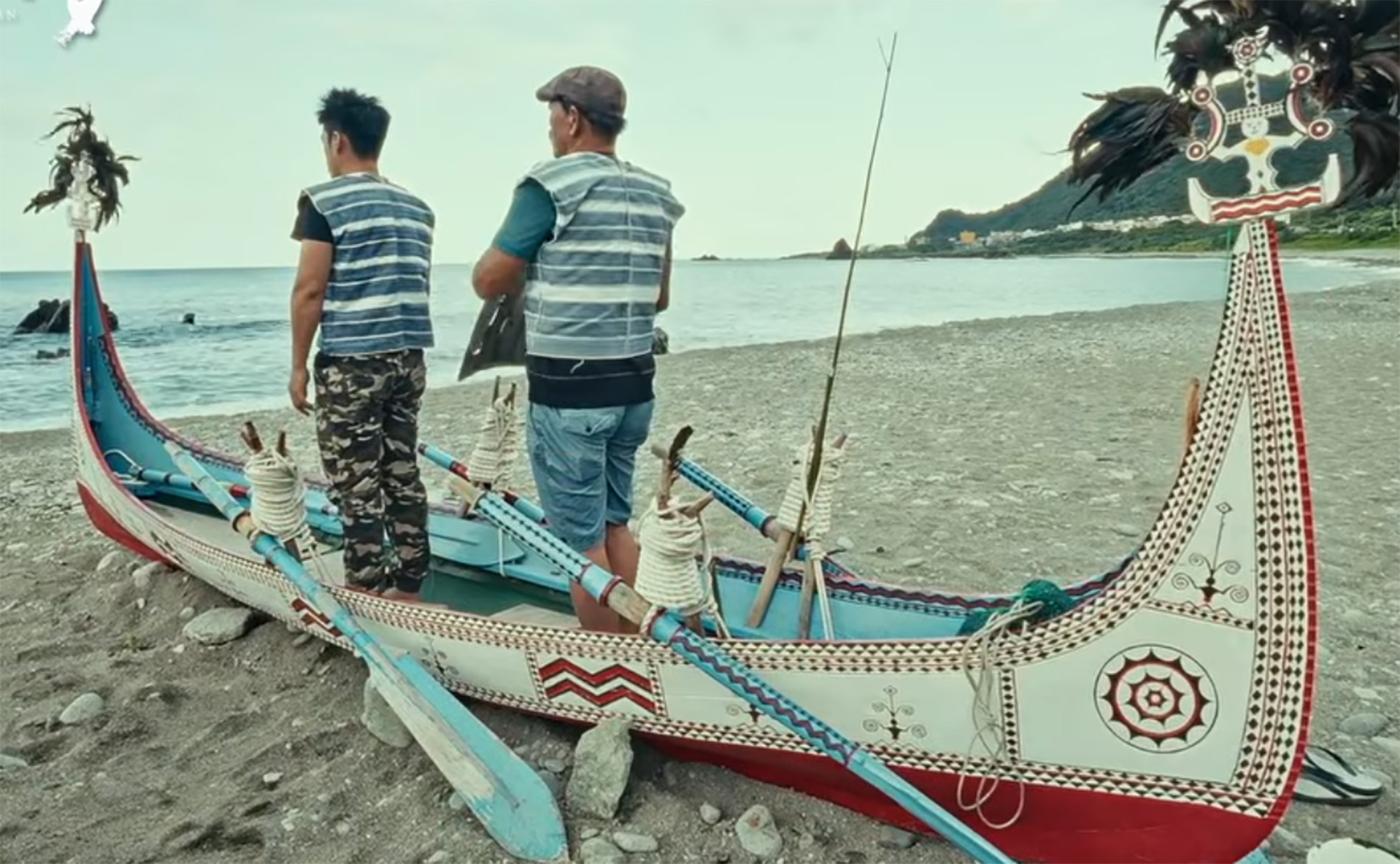 Two men standing in an ornately decorated watercraft on a beach by the sea.