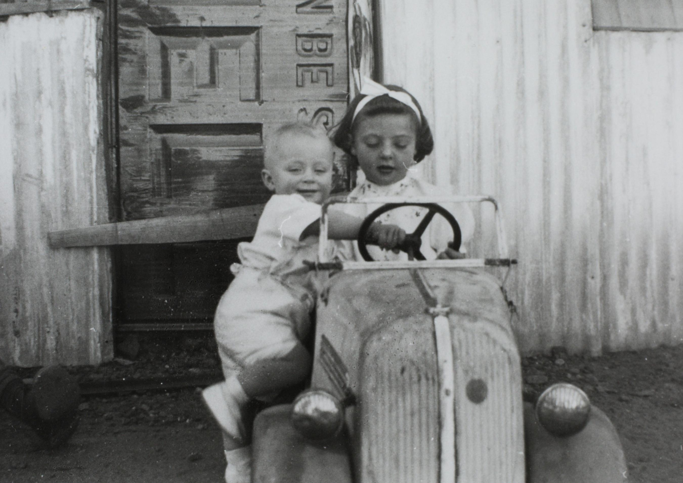 Black and white photograph of two children playing on a toy car.