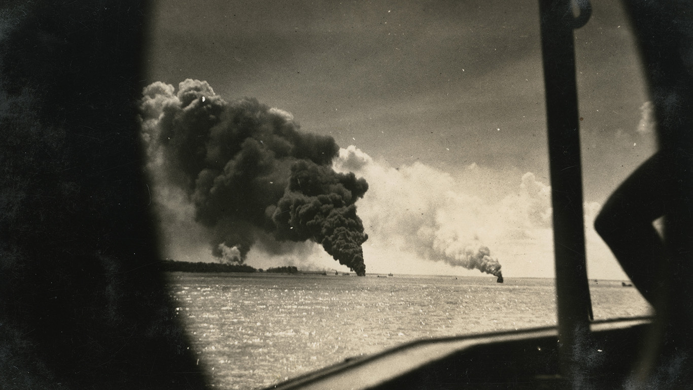 Black and white photograph of black and white plumes of smoke coming from boats on the water.