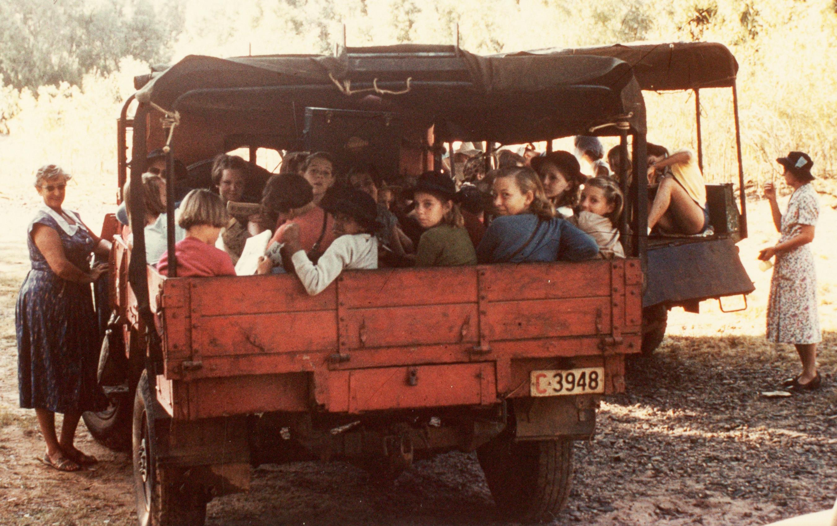 Photograph of children sitting in the tray back of a red utility truck.