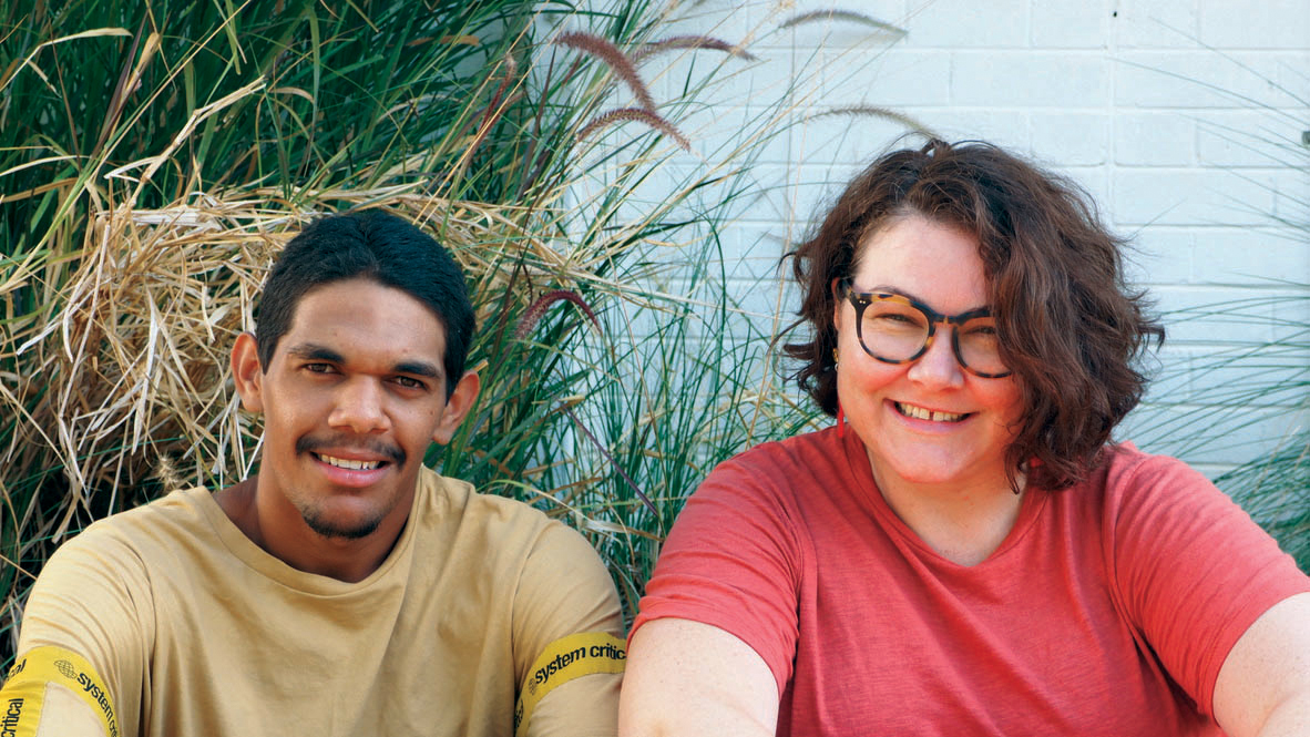 Man and woman sitting down in front of shrubbery