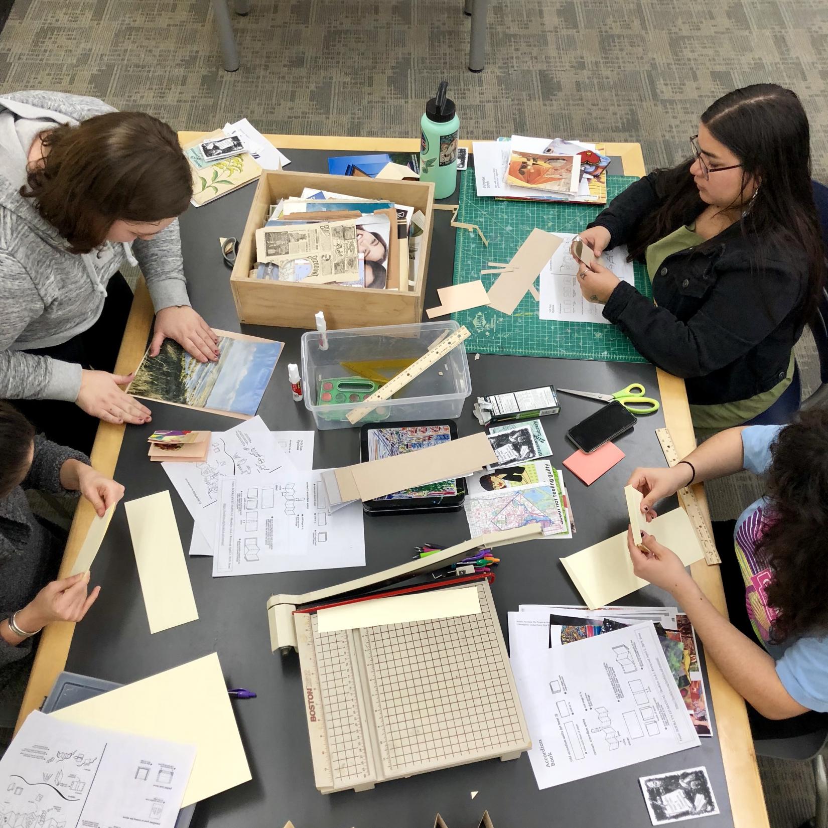 4 people sitting around a table with craft equipment making their own magazine