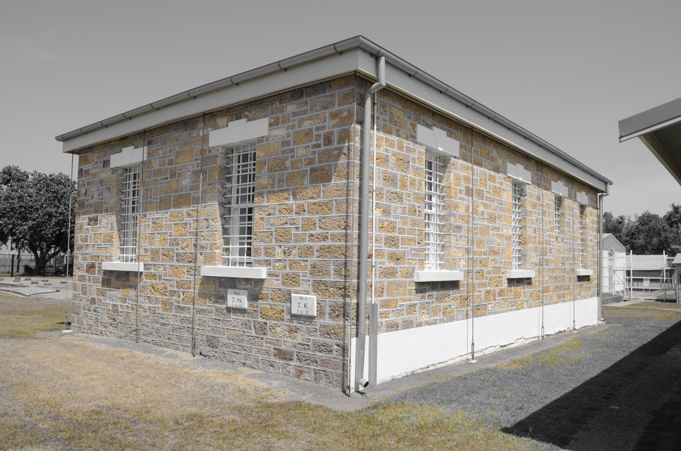 Picture of Fannie Bay Gaol building - square building with orange stone blocks. Background colour edited to grey in order to make the building stand out more. 