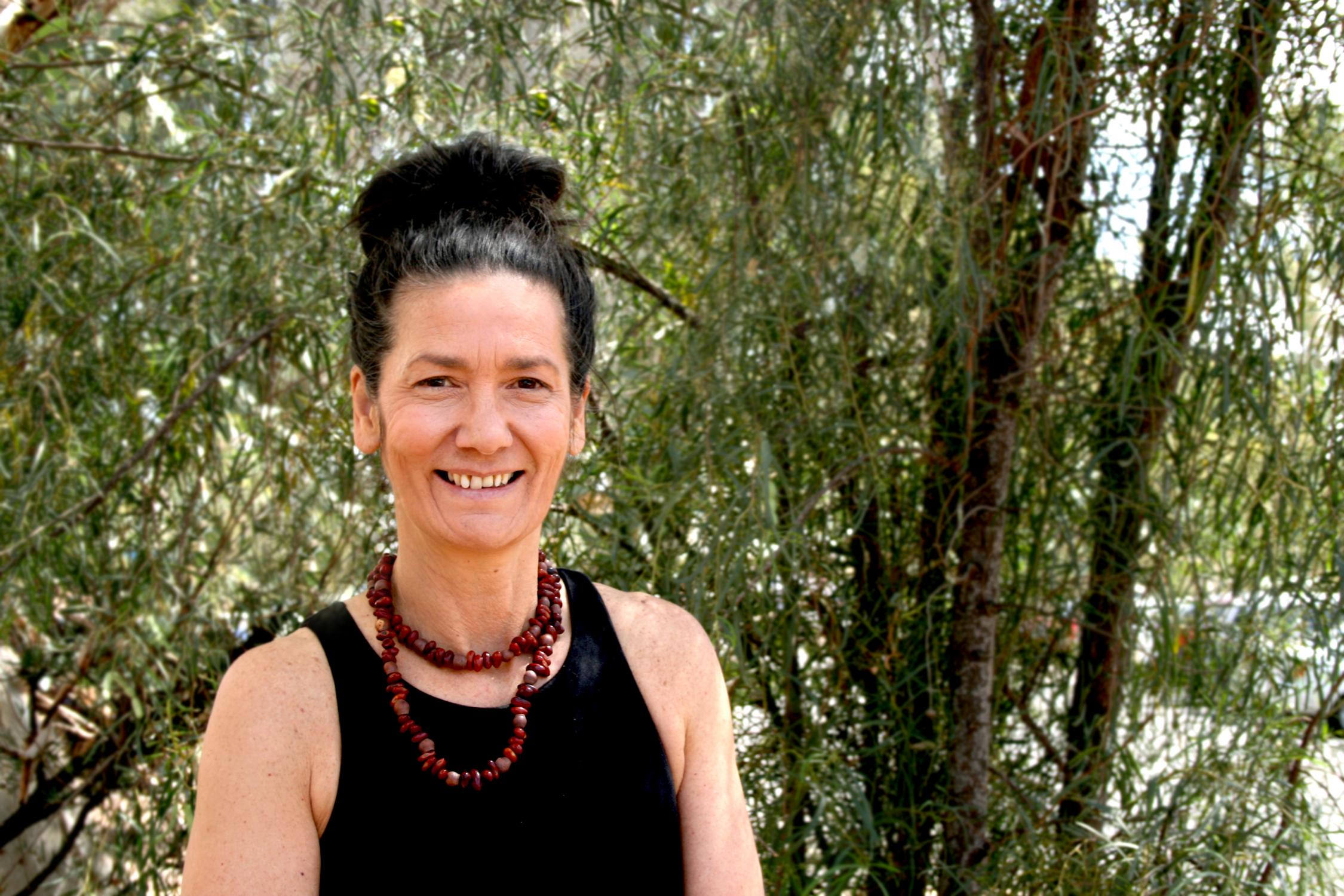 Picture of woman in a black singlet, standing in front of green trees. 