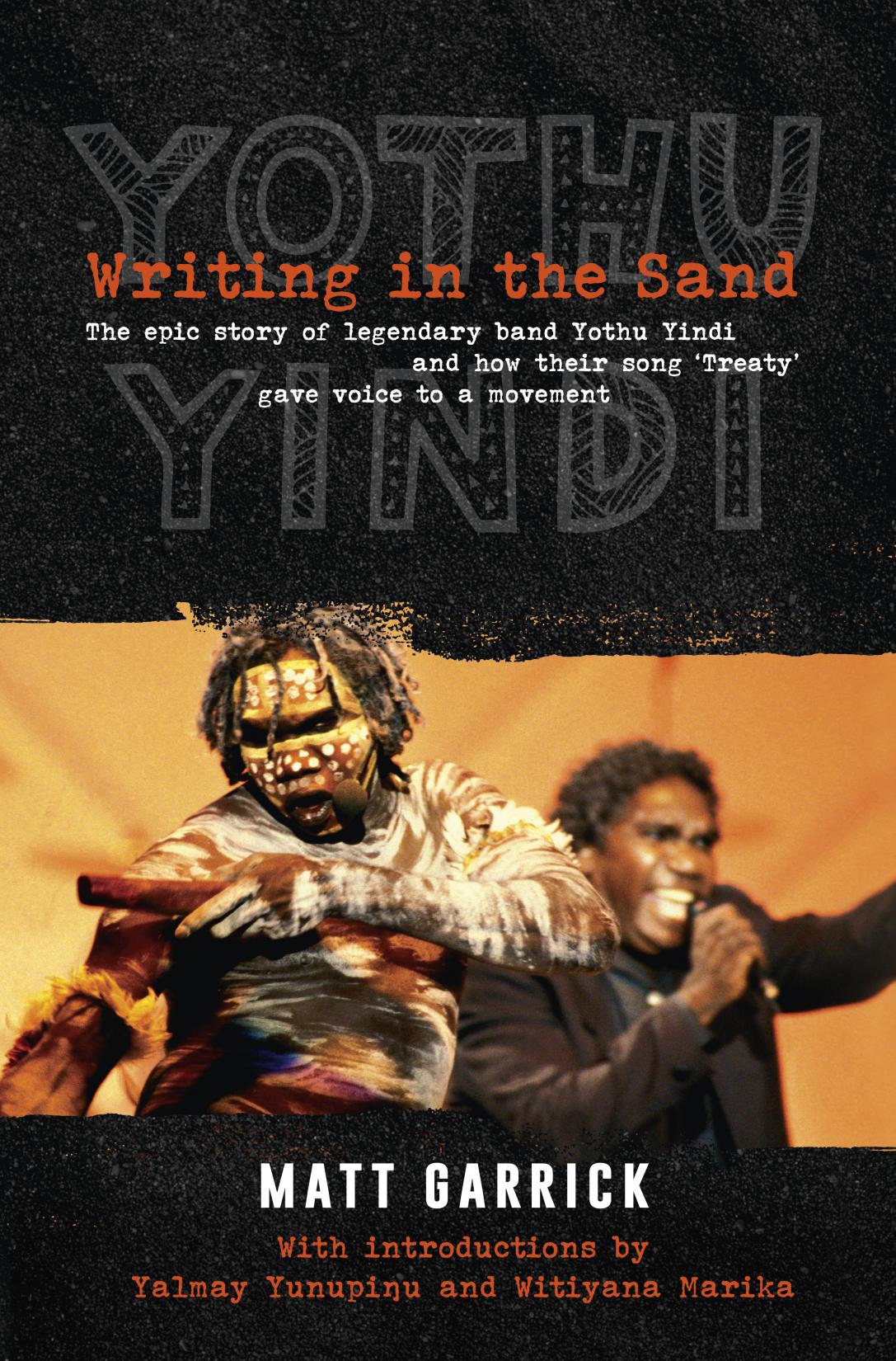 Cover of the book. Top has writing 'Writing in the sand' in big red font. below that in white smaller font it has 'the epic story of legendary band yothu yindi and how their song treaty gave voice to a movement'. the words Yothu Yindi are behind this writing in faint grey text. Image of M Yuninpingu and another Aboriginal dancer in traditional dress are below the text. 