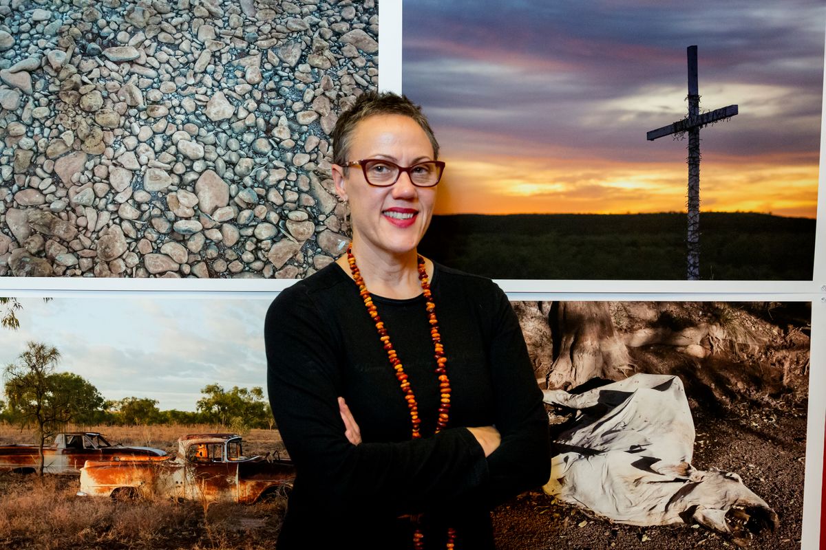 Picture of middle aged woman standing in front of four bright images behind her. 