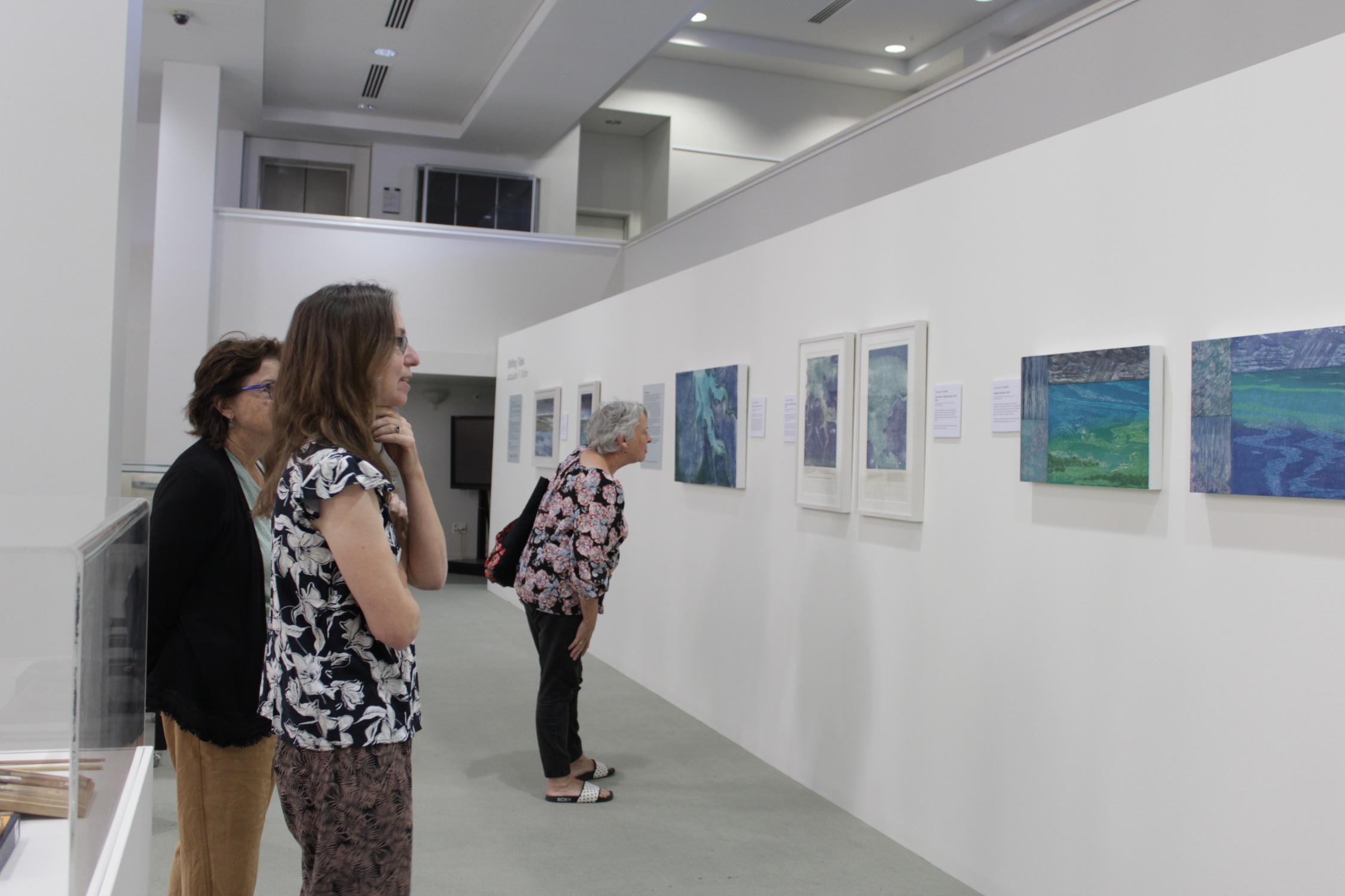 Image of three women standing in a small gallery space looking at artworks on the wall