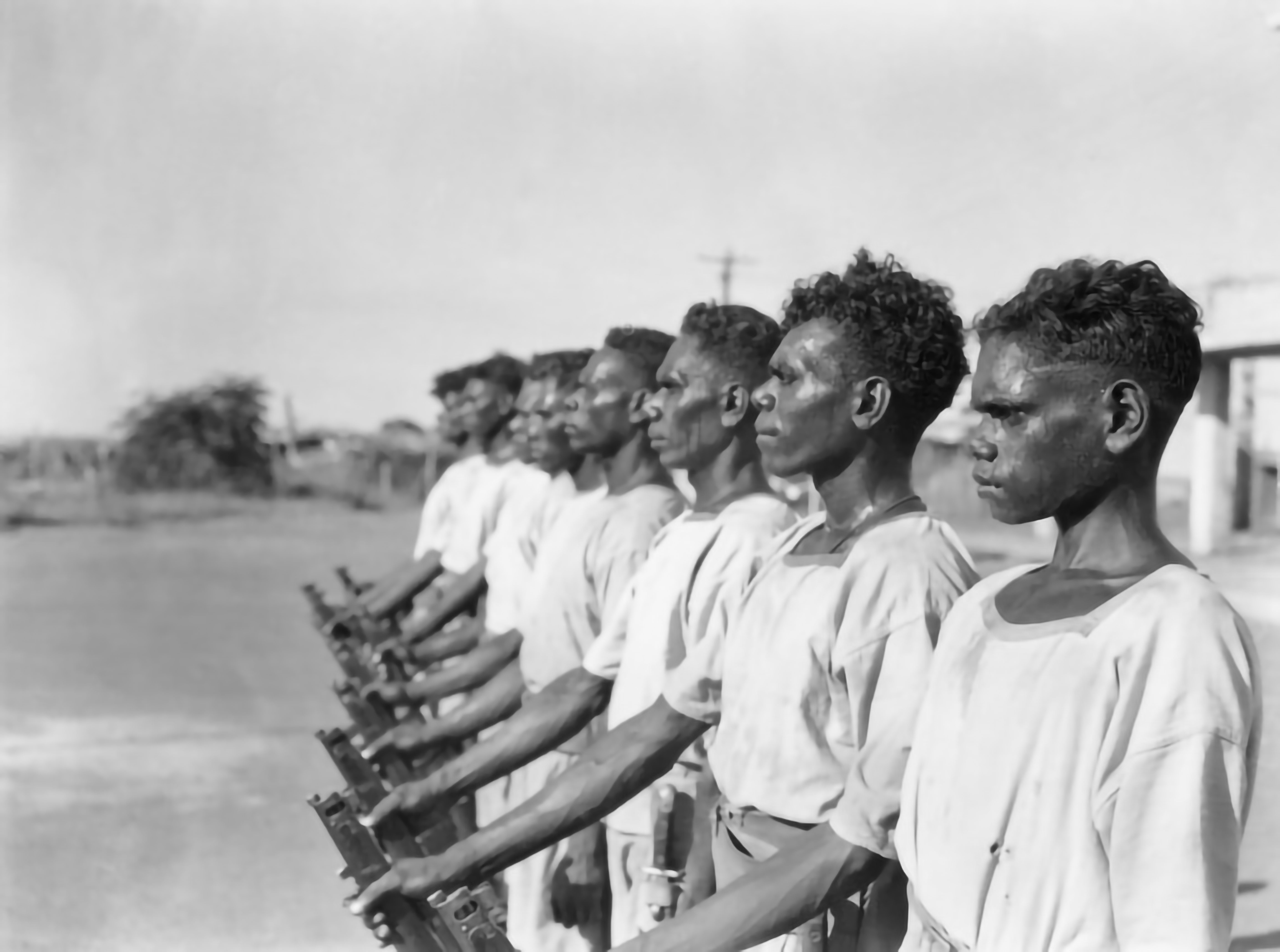 Black and white picture of 8 black serviceman in white tunic uniform standing in a line holding their rifle in their right hand