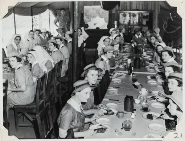 n Sisters Mess. Five large tables placed end to end with nurses seated around and eating a meal together. 