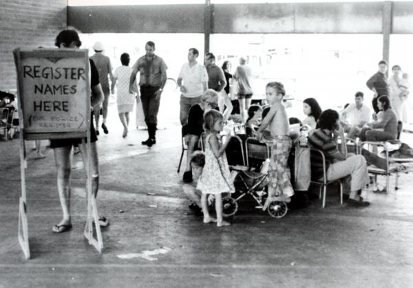 Registration area for evacuees after Cyclone Tracy. Photo shows a registration board and several people waiting around. Casuarina High School 