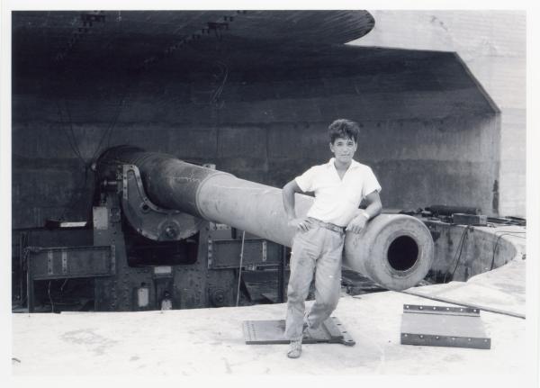A young member of the Fujita Salvage Company leans against a 9.2-inch counter-bombardment gun at East Point.