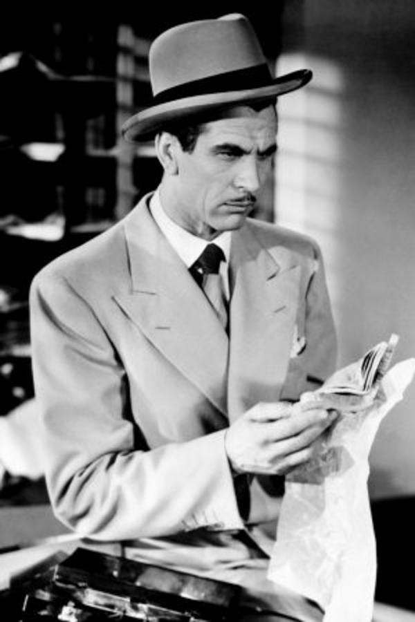 A man with a pencil-thin moustache and dressed in a grey suit and homburg inspects a piece of evidence.
