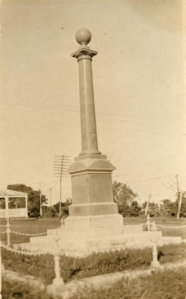 The Cenotaph stands at centre with a low chain fence and in background is the corner of the administration office and a slightly crooked power pole.