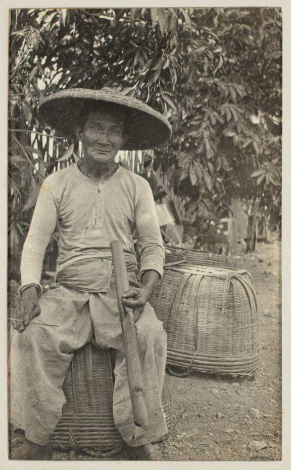 Man wearing a cane hat and sitting on a basket 