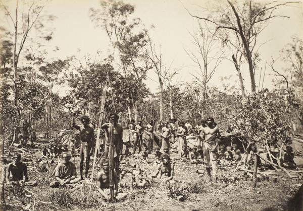Depicts a group of Aboriginal women, men and children in a camp setting in the bush.