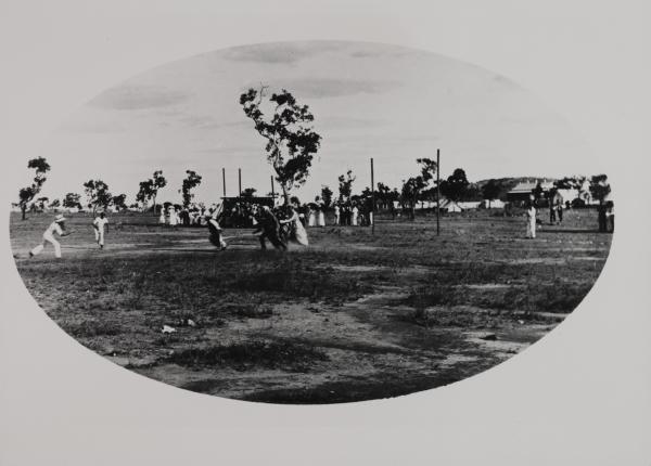 Blurred image of half a dozen distant figures in various costumes on a sporting field with small crowd in background.