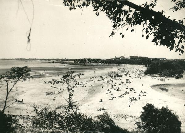 Photograph from afar of people on the sandy beach by the water.