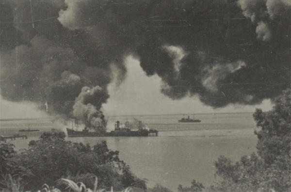 Photograph of ships on the water with smoke billowing following bombing.