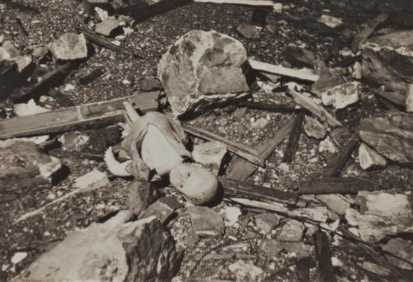 Photograph of doll amongst debris following bombing.