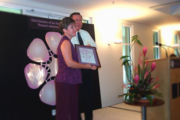 Former Chief Minister, Denis Burke, presents Amanda Mouthaan with a certificate in a frame for the Chief Minister's Women's Achievement Awards.