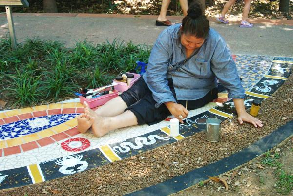 Gulumerrdjin/Larrakia artist June Mills painting on the mosaic tile path.