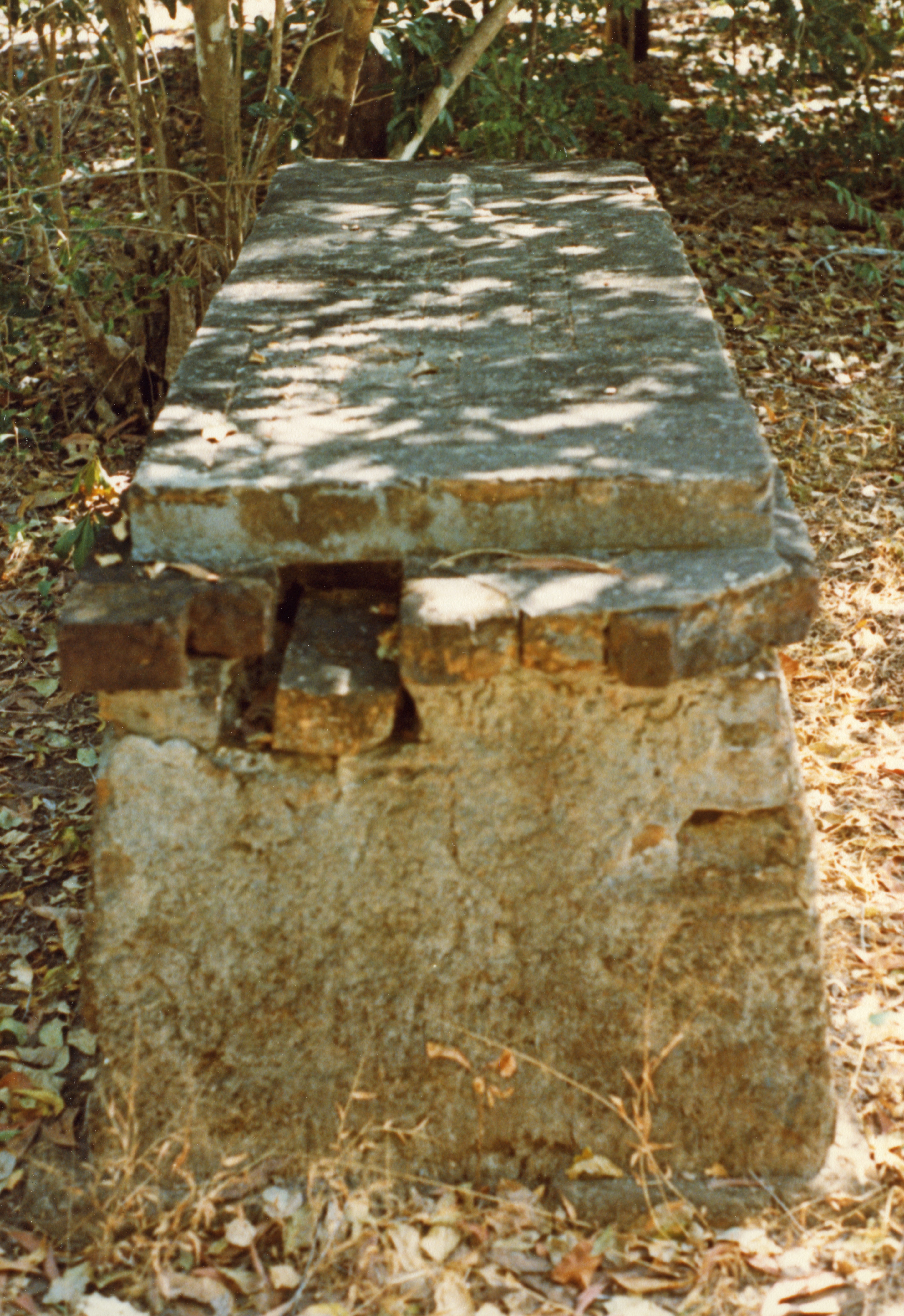 Depicts an above-ground brick tomb with cross on top.