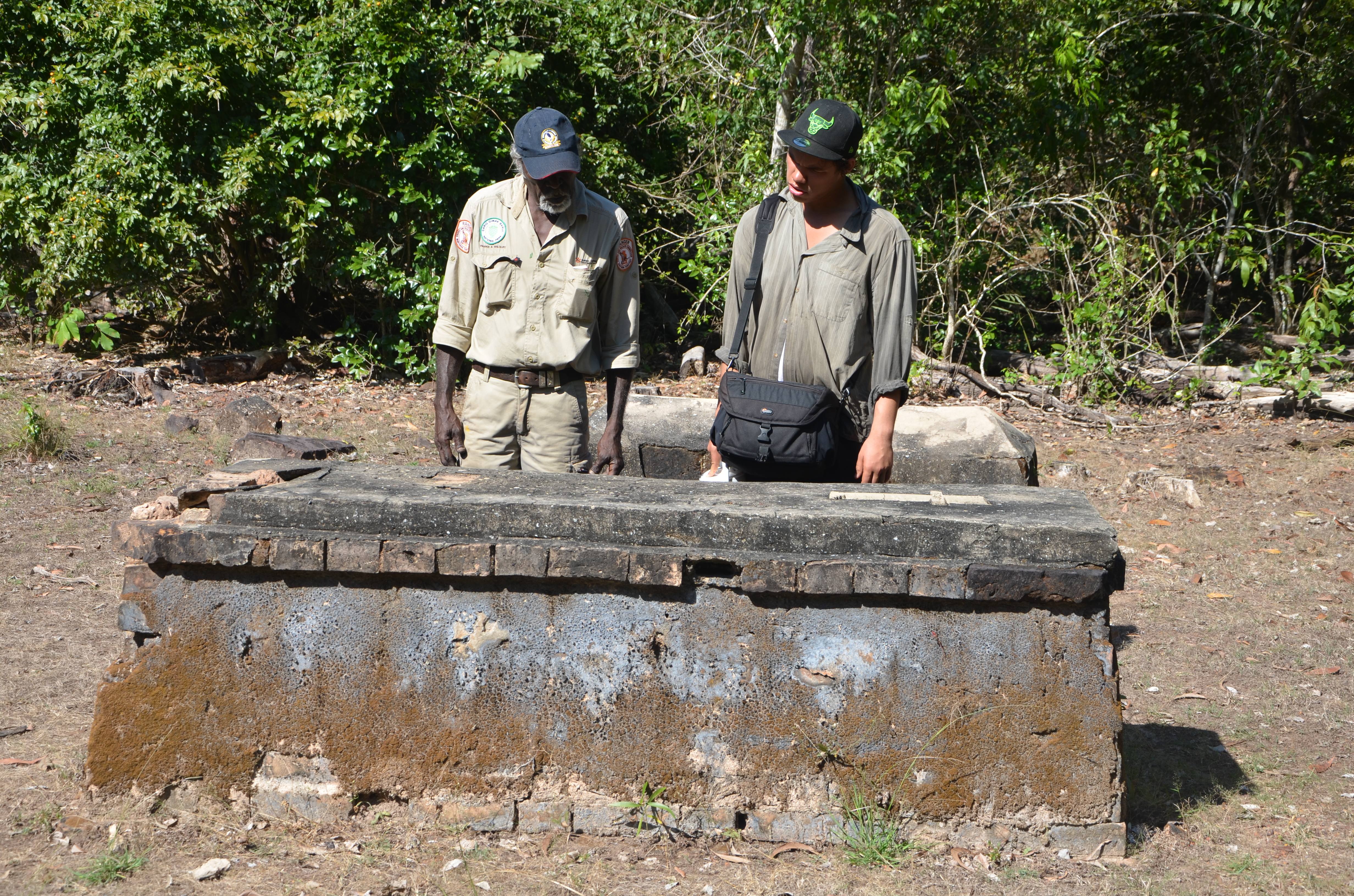 Depicts two Aboriginal men inspecting an above-ground brick tomb.